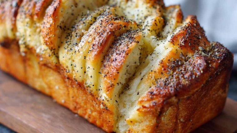 Golden pull-apart bread layered with lemon glaze and sprinkled with poppy seeds, served on a rustic plate.