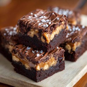 Rich SNICKERS brownies topped with caramel, peanuts, and chocolate chunks on a dessert plate