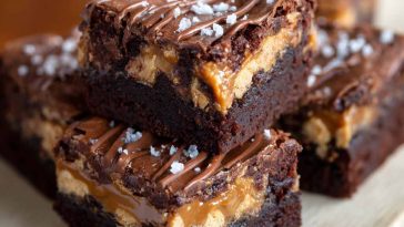 Rich SNICKERS brownies topped with caramel, peanuts, and chocolate chunks on a dessert plate