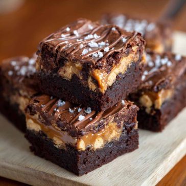 Rich SNICKERS brownies topped with caramel, peanuts, and chocolate chunks on a dessert plate