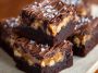Rich SNICKERS brownies topped with caramel, peanuts, and chocolate chunks on a dessert plate