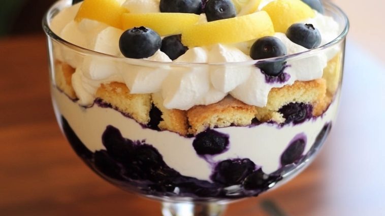 Layered lemon blueberry trifle with fluffy whipped cream, fresh blueberries, and lemon zest served in a glass dish.