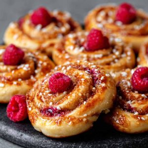Freshly baked sugar raspberry Danish buns topped with glaze and filled with sweet raspberry jam.