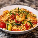 Shrimp and vegetable tomato orzo served in a bowl with herbs