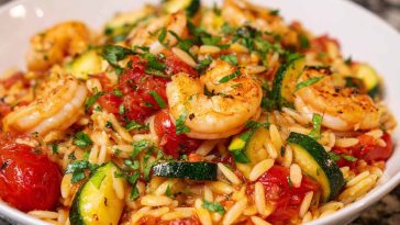 Shrimp and vegetable tomato orzo served in a bowl with herbs