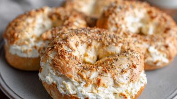 A batch of golden brown cottage cheese protein bagels made with only three ingredients, fresh out of the air fryer, served on a wooden board.