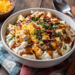 Ultimate loaded chicken and gravy mashed potato bowls topped with melted cheese, corn, and fresh herbs served in a rustic dish