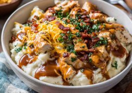 Ultimate loaded chicken and gravy mashed potato bowls topped with melted cheese, corn, and fresh herbs served in a rustic dish