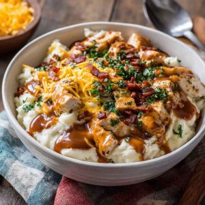 Ultimate loaded chicken and gravy mashed potato bowls topped with melted cheese, corn, and fresh herbs served in a rustic dish