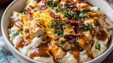 Ultimate loaded chicken and gravy mashed potato bowls topped with melted cheese, corn, and fresh herbs served in a rustic dish