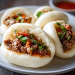 Freshly baked meat buns filled with savory ground meat and vegetables, served warm on a wooden board.