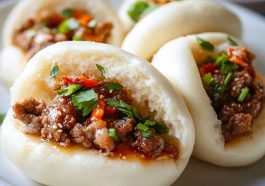 Freshly baked meat buns filled with savory ground meat and vegetables, served warm on a wooden board.