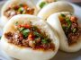 Freshly baked meat buns filled with savory ground meat and vegetables, served warm on a wooden board.