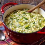 A warm bowl of creamy orzo, leek, and dill soup garnished with fresh herbs, served in a rustic dish.
