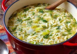 A warm bowl of creamy orzo, leek, and dill soup garnished with fresh herbs, served in a rustic dish.