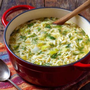 A warm bowl of creamy orzo, leek, and dill soup garnished with fresh herbs, served in a rustic dish.