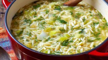 A warm bowl of creamy orzo, leek, and dill soup garnished with fresh herbs, served in a rustic dish.
