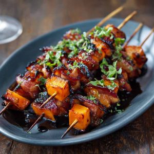 Candied sweet potato and bacon skewers glazed with a sticky brown sugar sauce, roasted until caramelized and crispy, served on wooden skewers.