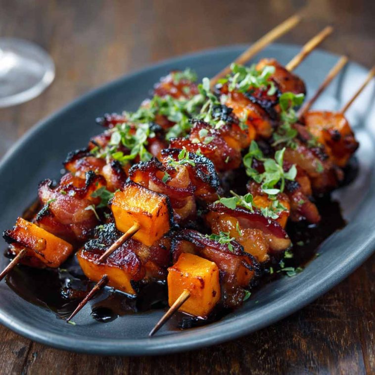Candied sweet potato and bacon skewers glazed with a sticky brown sugar sauce, roasted until caramelized and crispy, served on wooden skewers.