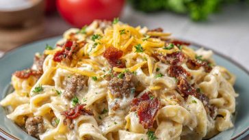Creamy Alfredo pasta loaded with ground beef, crispy bacon, and melted cheese, garnished with herbs in a skillet.