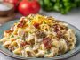 Creamy Alfredo pasta loaded with ground beef, crispy bacon, and melted cheese, garnished with herbs in a skillet.