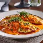 Flaky tilapia fillets in a rich roasted red pepper sauce, garnished with herbs and served in a skillet for a quick and flavorful meal.