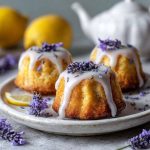 Mini lemon cakes topped with lavender glaze and fresh lemon zest on a dessert plate.