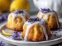 Mini lemon cakes topped with lavender glaze and fresh lemon zest on a dessert plate.