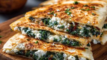 Golden Mediterranean quesadillas filled with fresh spinach, creamy feta cheese, and herbs, sliced and served on a wooden board.