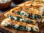 Golden Mediterranean quesadillas filled with fresh spinach, creamy feta cheese, and herbs, sliced and served on a wooden board.