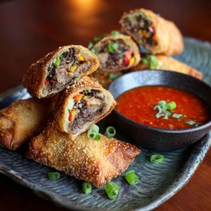 Voodoo Egg Rolls with crispy golden wrappers, filled with savory ingredients, served with spicy dipping sauce.