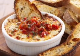 Bubbly three‑cheese tomato bruschetta dip baked in a skillet, topped with fresh basil and served with toasted bread slices.