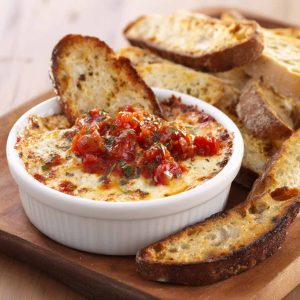 Bubbly three‑cheese tomato bruschetta dip baked in a skillet, topped with fresh basil and served with toasted bread slices.