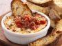 Bubbly three‑cheese tomato bruschetta dip baked in a skillet, topped with fresh basil and served with toasted bread slices.