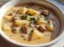 Hearty sausage potato soup served in a rustic bowl with carrots, celery, and fresh herbs in a creamy broth.