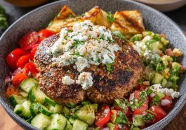 Mediterranean burger bowl with seasoned beef, fresh vegetables, hummus, feta cheese, and tzatziki sauce served in a rustic bowl.