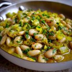 Flavorful butter beans with sautéed leeks served in a rustic bowl, garnished with fresh herbs and olive oil.