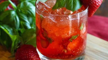 Refreshing strawberry basil smash cocktail made with fresh strawberries, basil leaves, lime juice, and ice in a glass, garnished with herbs and fruit.