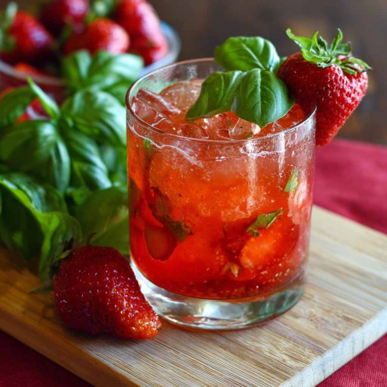 Refreshing strawberry basil smash cocktail made with fresh strawberries, basil leaves, lime juice, and ice in a glass, garnished with herbs and fruit.