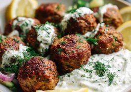 Baked Greek lentil meatballs served with creamy tzatziki sauce, fresh herbs, and a side of vegetables.