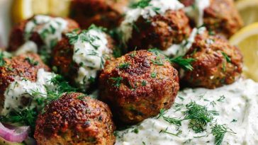 Baked Greek lentil meatballs served with creamy tzatziki sauce, fresh herbs, and a side of vegetables.