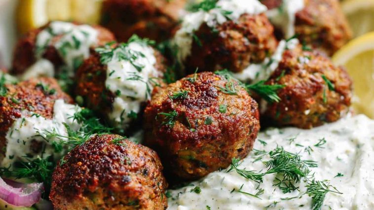 Baked Greek lentil meatballs served with creamy tzatziki sauce, fresh herbs, and a side of vegetables.