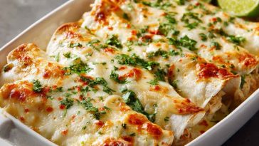 Creamy white rotisserie chicken enchiladas baked in a rich white sauce, topped with melted cheese and fresh herbs in a casserole dish.