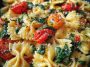 Colorful tomato spinach farfalle pasta served in a bowl with fresh basil, parmesan, and a light garlic sauce.