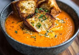 "Velvety roasted red pepper Gouda soup served in a bowl with fresh herbs and crusty bread"