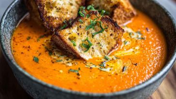"Velvety roasted red pepper Gouda soup served in a bowl with fresh herbs and crusty bread"