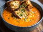 "Velvety roasted red pepper Gouda soup served in a bowl with fresh herbs and crusty bread"