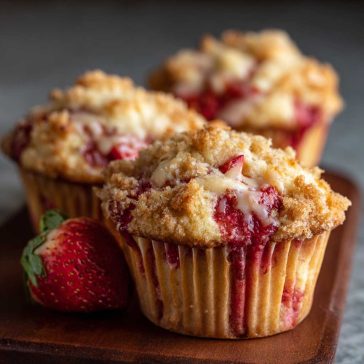 Freshly baked strawberry cream cheese muffins with golden tops and chunks of strawberries on a cooling rack