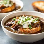 French onion short rib soup topped with melted Gruyère toast served in a rustic bowl with caramelized onions and herbs