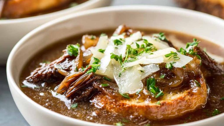 French onion short rib soup topped with melted Gruyère toast served in a rustic bowl with caramelized onions and herbs
